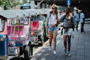 Two girls strolling by a line of parked tuk tuks, laughing and having fun